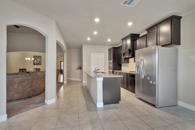 kitchen with light tile patterned flooring, backsplash, sink, an island with sink, and stainless steel fridge