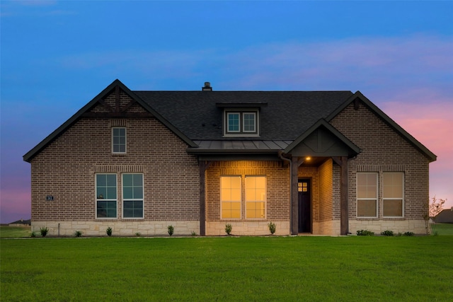 view of front of home featuring metal roof, roof with shingles, a standing seam roof, a front lawn, and brick siding