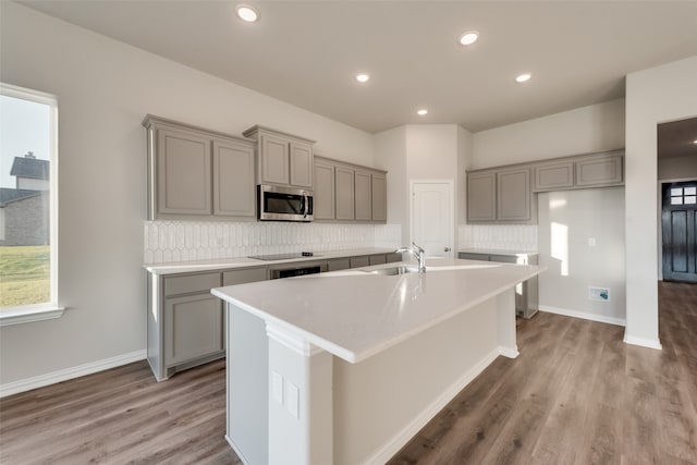 kitchen featuring hardwood / wood-style floors, an island with sink, gray cabinets, and tasteful backsplash