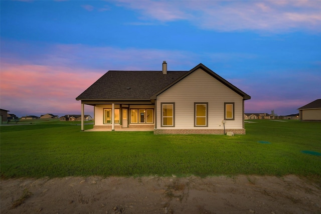 back house at dusk featuring a lawn