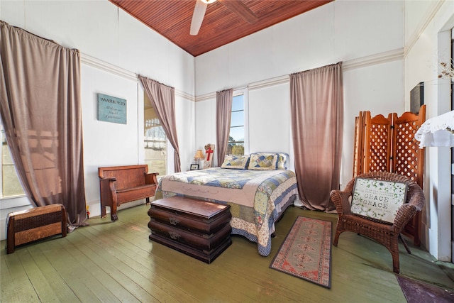 bedroom featuring ceiling fan, multiple windows, a towering ceiling, and hardwood / wood-style floors