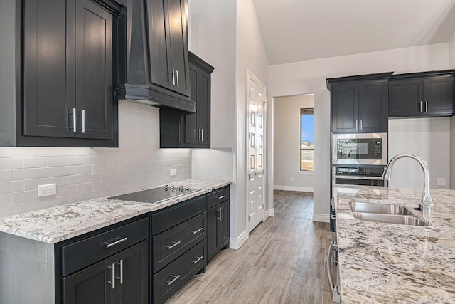 kitchen with decorative backsplash, black electric stovetop, light wood-type flooring, sink, and stainless steel microwave