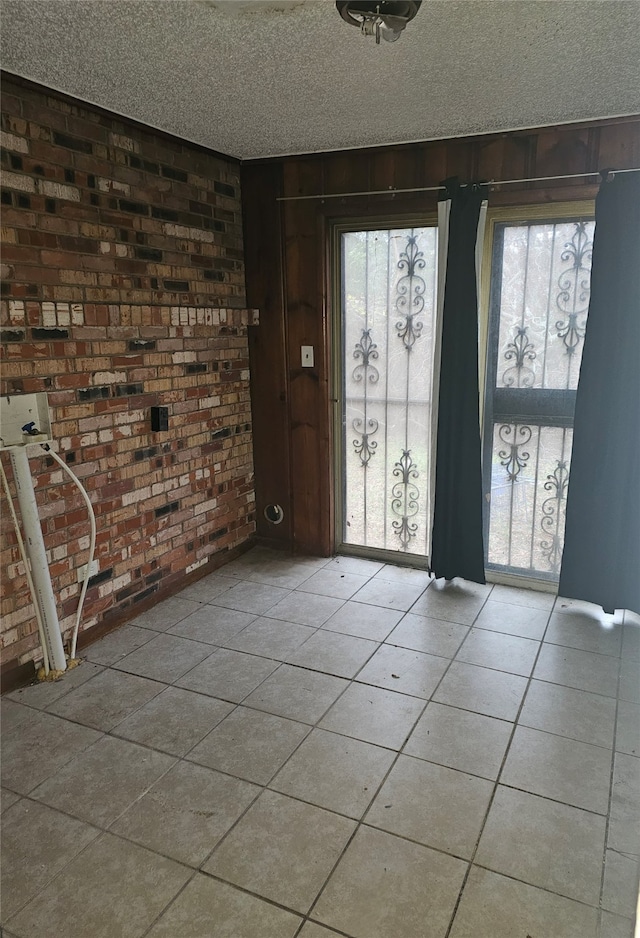 spare room featuring a textured ceiling, light tile patterned flooring, and brick wall