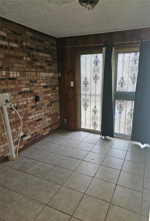 entrance foyer with a wealth of natural light, brick wall, light tile patterned floors, and a textured ceiling