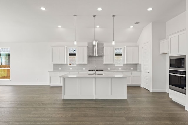 kitchen featuring decorative light fixtures, a center island with sink, white cabinetry, stainless steel oven, and wall chimney exhaust hood