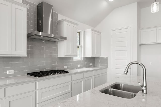 kitchen featuring decorative light fixtures, wall chimney range hood, vaulted ceiling, white cabinets, and sink