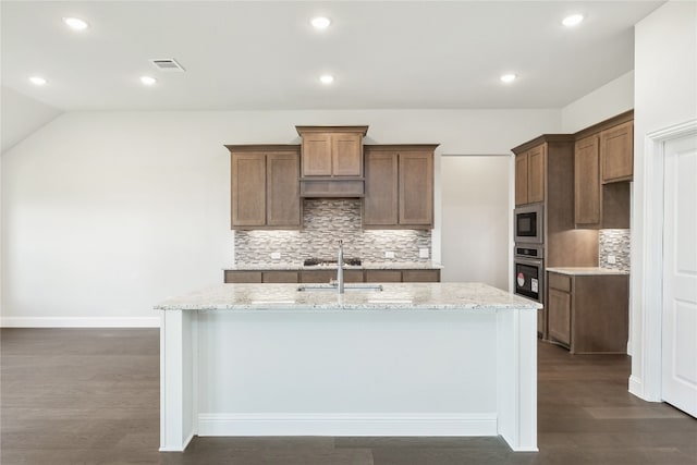 kitchen featuring light stone counters, stainless steel appliances, dark wood-type flooring, visible vents, and an island with sink