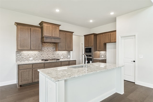 kitchen with light stone counters, dark wood-type flooring, a sink, appliances with stainless steel finishes, and tasteful backsplash