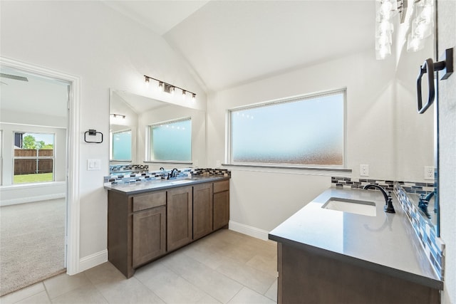 full bath with two vanities, decorative backsplash, vaulted ceiling, a sink, and baseboards