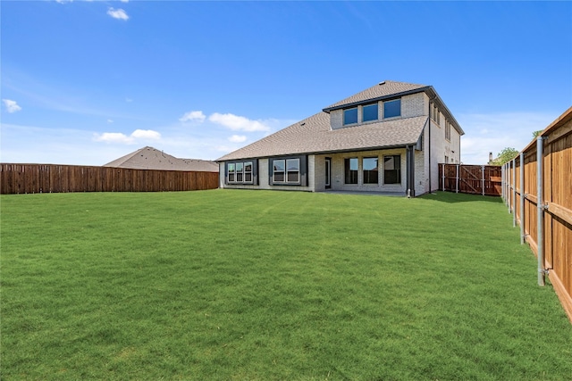 back of house with a fenced backyard, a lawn, and brick siding