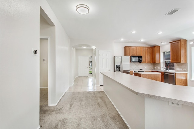 kitchen with lofted ceiling, backsplash, light colored carpet, kitchen peninsula, and stainless steel appliances