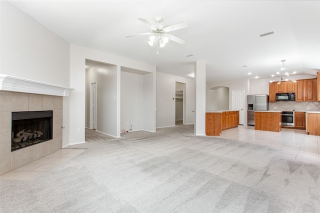 unfurnished living room featuring a tile fireplace, ceiling fan with notable chandelier, and light colored carpet