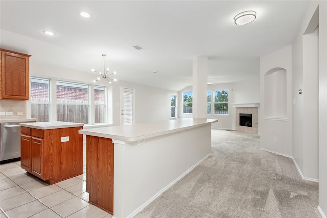 kitchen featuring light carpet, an inviting chandelier, stainless steel dishwasher, a fireplace, and a kitchen island