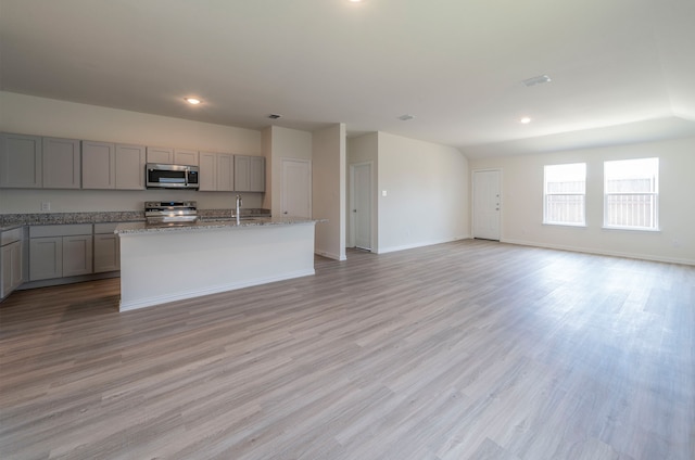 kitchen with range, a kitchen island with sink, light wood-type flooring, and gray cabinetry