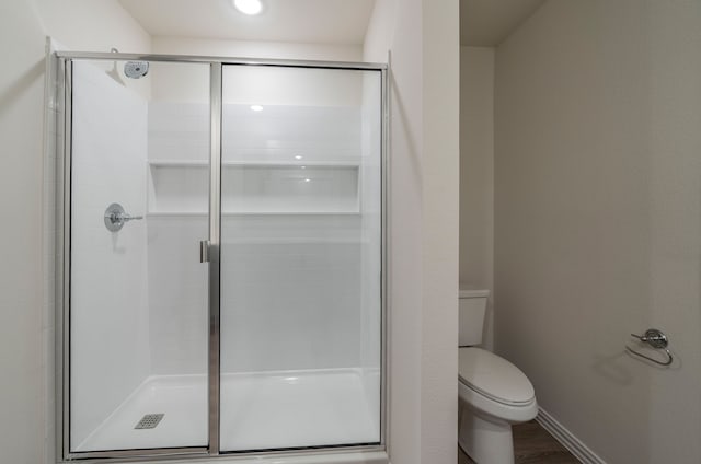 bathroom with hardwood / wood-style flooring, a shower with door, and toilet