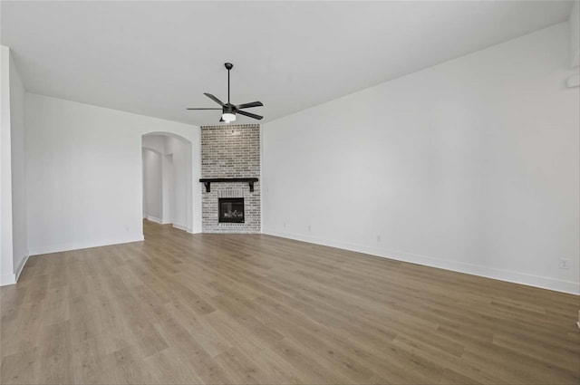 unfurnished living room featuring ceiling fan, brick wall, light wood-type flooring, and a brick fireplace