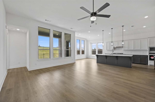 unfurnished living room featuring a healthy amount of sunlight, wood-type flooring, sink, and ceiling fan