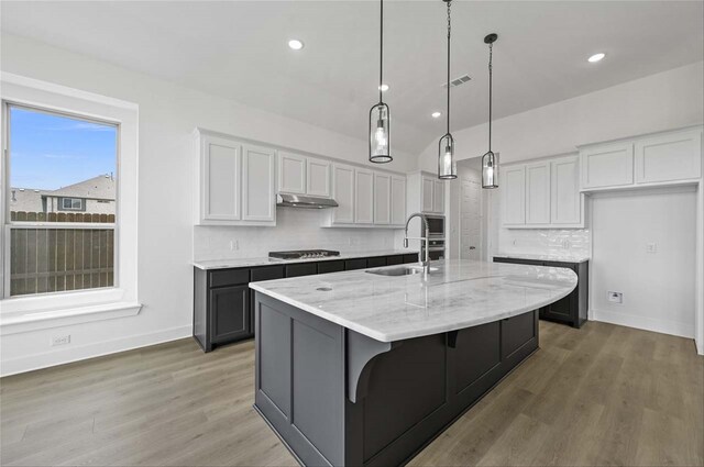 kitchen with gas cooktop, light hardwood / wood-style flooring, tasteful backsplash, white cabinets, and an island with sink