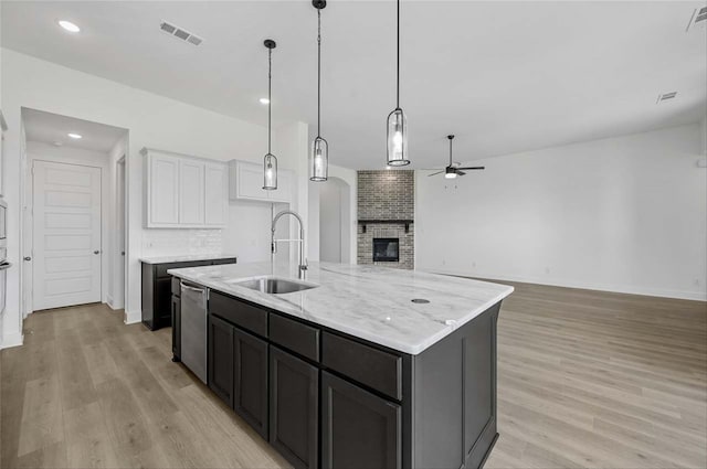 kitchen featuring white cabinets, sink, dishwasher, light hardwood / wood-style floors, and a brick fireplace