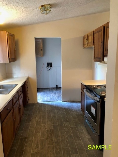 kitchen with dark hardwood / wood-style floors, a textured ceiling, stainless steel electric range oven, and sink