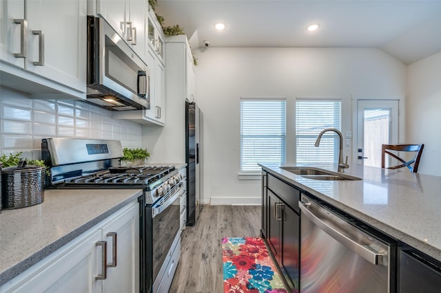 kitchen featuring tasteful backsplash, white cabinets, appliances with stainless steel finishes, light stone countertops, and a sink