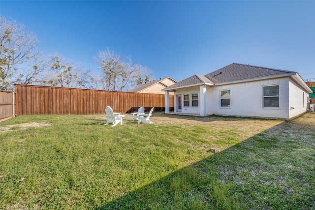 back of property featuring a yard, a fenced backyard, brick siding, and roof with shingles