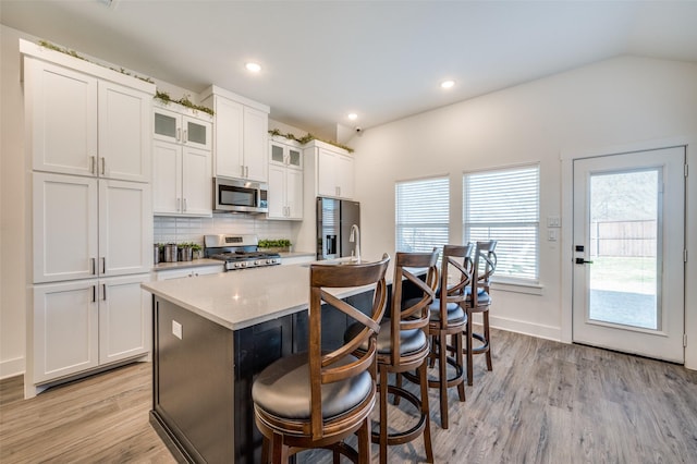 kitchen with a center island with sink, a breakfast bar area, tasteful backsplash, lofted ceiling, and appliances with stainless steel finishes