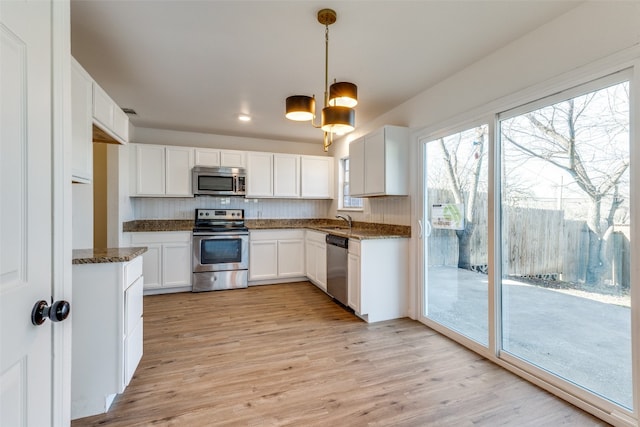 kitchen with appliances with stainless steel finishes, hanging light fixtures, white cabinetry, a chandelier, and light hardwood / wood-style flooring