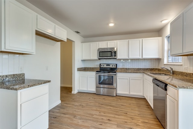 kitchen featuring stainless steel appliances, dark stone countertops, sink, white cabinetry, and light hardwood / wood-style flooring