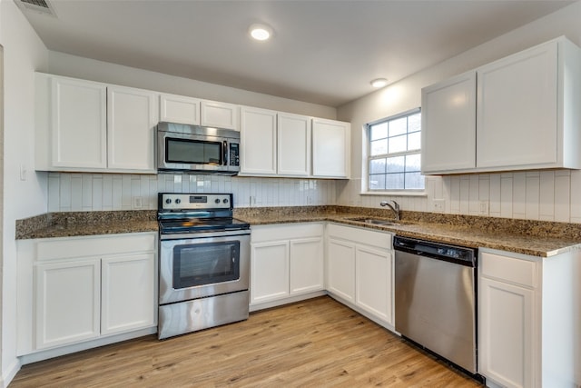 kitchen featuring sink, dark stone counters, white cabinets, stainless steel appliances, and light wood-type flooring