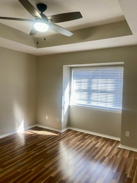 spare room featuring a raised ceiling, ceiling fan, and dark hardwood / wood-style flooring