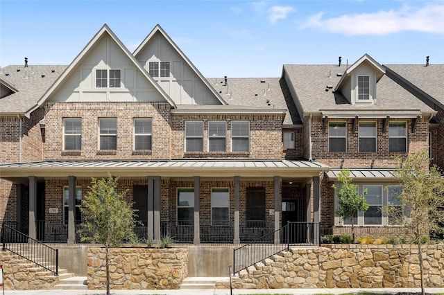 multi unit property with a standing seam roof, a porch, roof with shingles, brick siding, and stairs