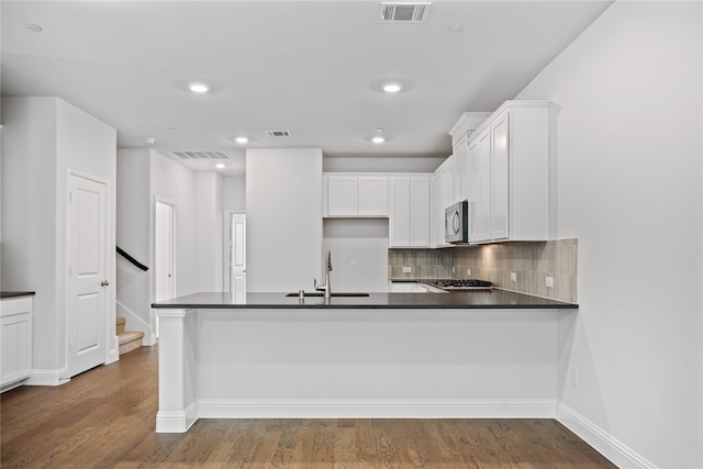 kitchen featuring tasteful backsplash, kitchen peninsula, sink, white cabinetry, and dark wood-type flooring