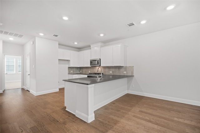 kitchen featuring kitchen peninsula, hardwood / wood-style floors, white cabinets, and tasteful backsplash