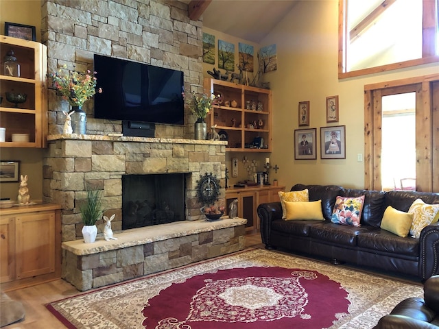 living area with high vaulted ceiling, beamed ceiling, wood finished floors, and a stone fireplace