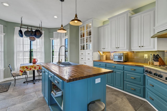 kitchen with butcher block countertops, sink, white cabinets, and a kitchen island with sink