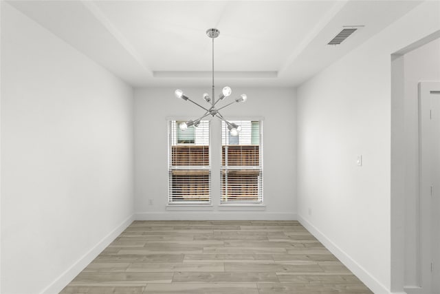 spare room with a chandelier, light wood-type flooring, and a tray ceiling