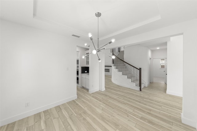 unfurnished dining area featuring light hardwood / wood-style flooring, a raised ceiling, and a chandelier