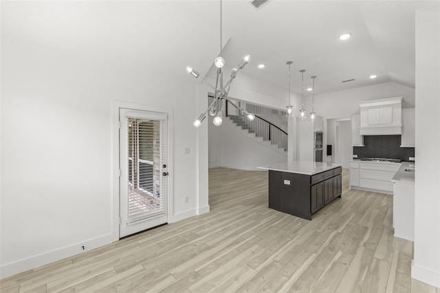 kitchen featuring a center island, hanging light fixtures, light wood-type flooring, white cabinetry, and tasteful backsplash