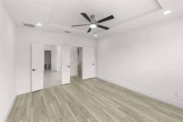 unfurnished bedroom featuring ceiling fan, light hardwood / wood-style flooring, and a tray ceiling