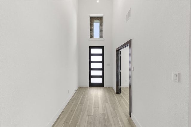 doorway to outside with a towering ceiling and light wood-type flooring