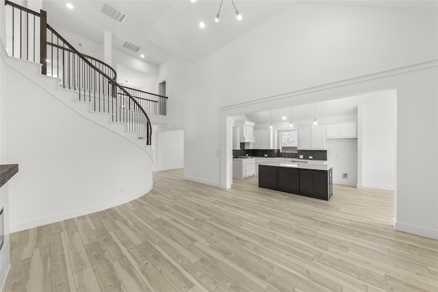 unfurnished living room featuring sink, light hardwood / wood-style floors, and a high ceiling