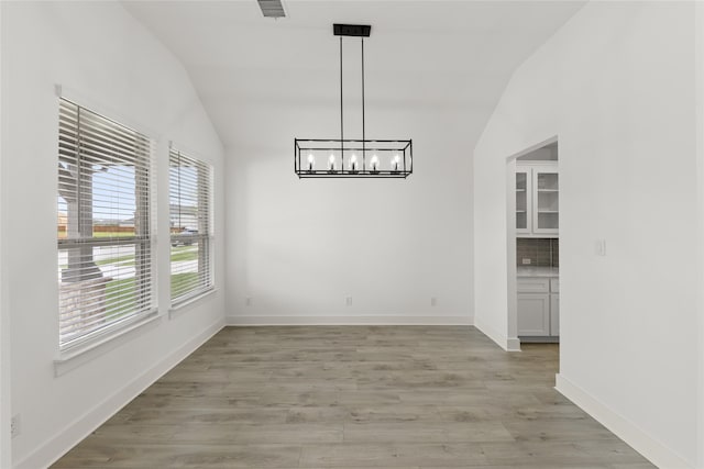 spare room with lofted ceiling, light wood-type flooring, and a notable chandelier