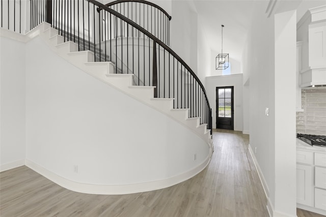 stairs with an inviting chandelier, light wood-type flooring, and a high ceiling