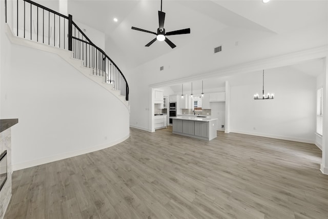 unfurnished living room featuring ceiling fan with notable chandelier, high vaulted ceiling, light hardwood / wood-style floors, and sink