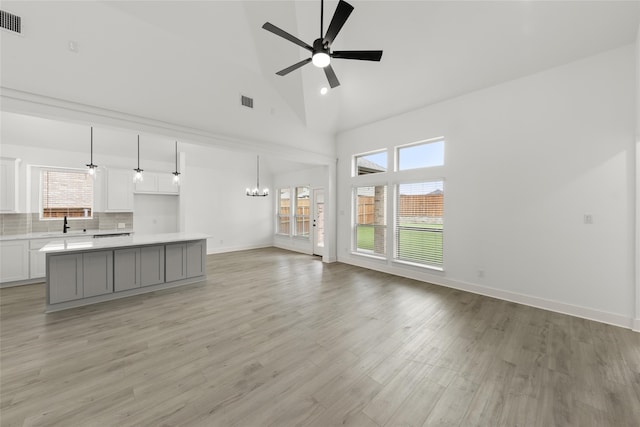 unfurnished living room with high vaulted ceiling, ceiling fan with notable chandelier, and light wood-type flooring