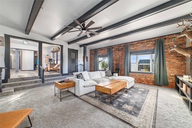 carpeted living room with beamed ceiling, ceiling fan, and brick wall