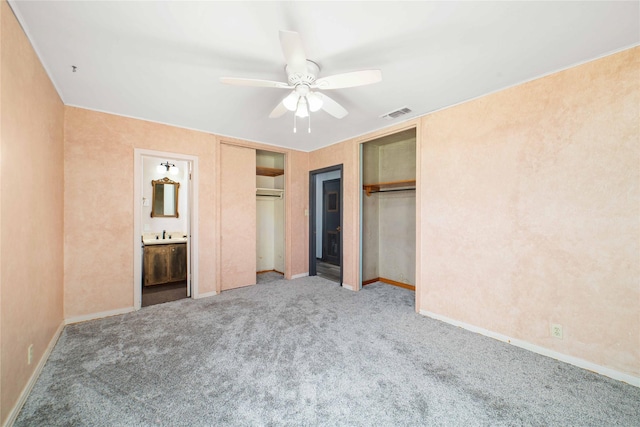 unfurnished bedroom with ensuite bath, ceiling fan, carpet floors, and two closets