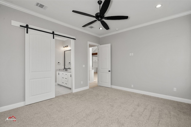 unfurnished bedroom featuring sink, light colored carpet, crown molding, a barn door, and ensuite bath