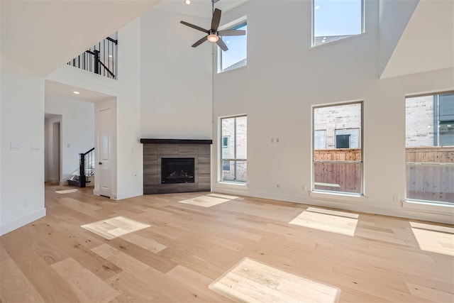 unfurnished living room featuring ceiling fan, a fireplace, a high ceiling, and light hardwood / wood-style flooring